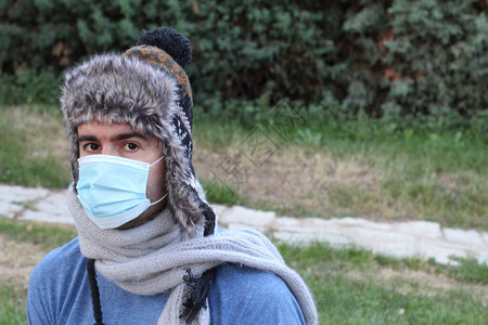 身戴面具的英俊青年男子在绿公园保护他人和取暖衣图片