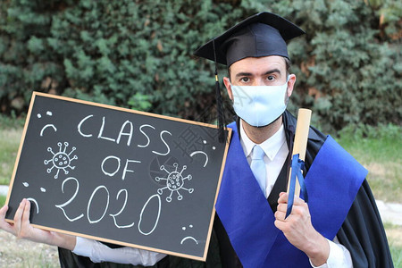 英俊的年轻学生毕业服装有滚版文凭和黑板图片