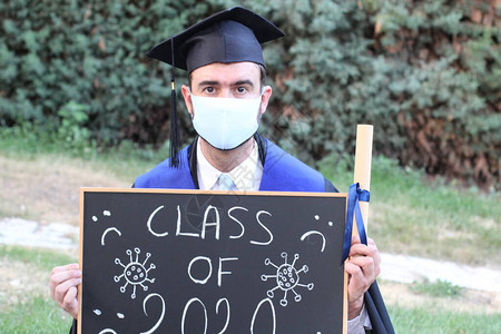 英俊的年轻学生毕业服装有滚版文凭和黑板背景图片