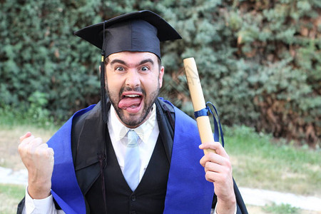 英俊的青年学生穿着毕业服装在公园获得滚版文凭的背景图片