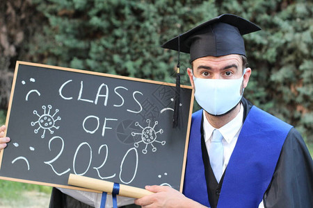 英俊的年轻学生毕业服装有滚版文凭和黑板背景图片