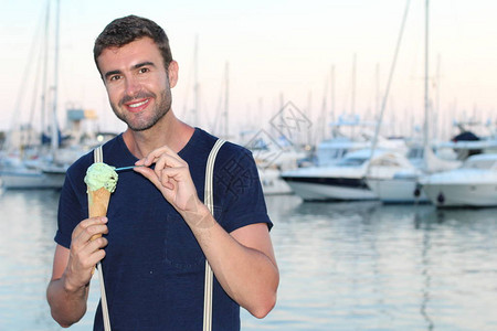 穿着时装的英俊年轻男子在日落时在游艇前港口吃冰淇淋图片