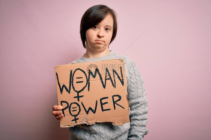 年轻患有综合症的年轻女在粉红背景上举着妇女权力抗争横幅图片