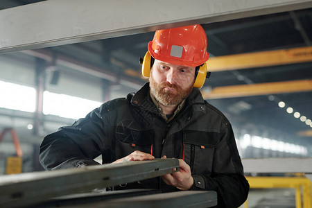 戴防护头盔和耳机的留着胡子的年轻工程师处理工业机器图片