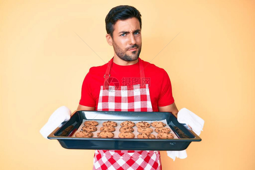 穿着面包师制服的西班牙年轻人拿着自制饼干持怀疑和紧张态度图片