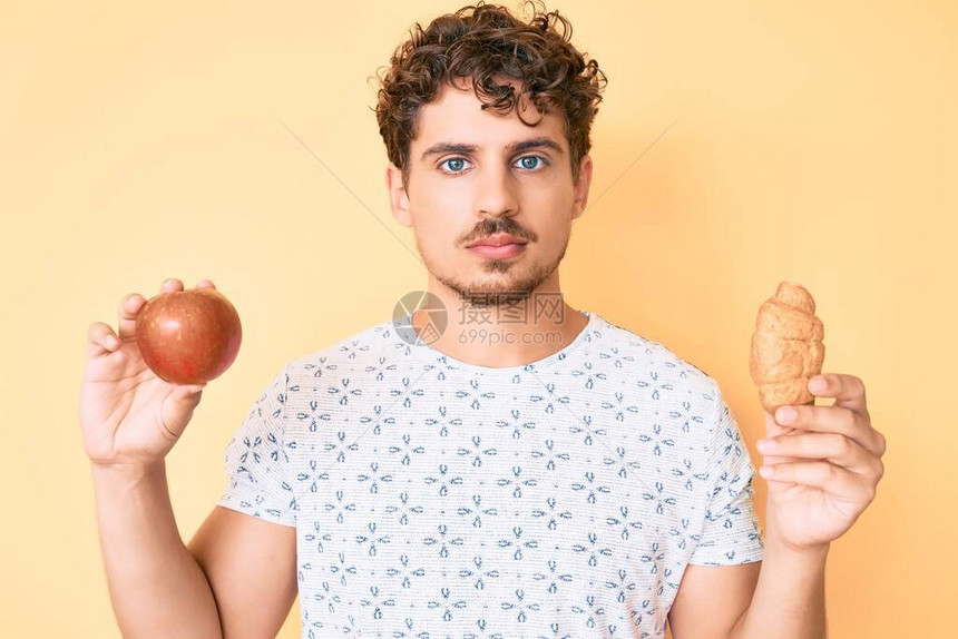 有卷发的年轻caucasian男子拿着苹果和羊角面包放松图片