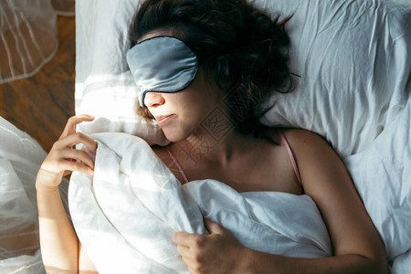 早上睡在床上戴面具的女人脸上明亮的光线图片