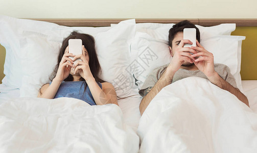 已婚年轻夫妇用手机躺在床上图片