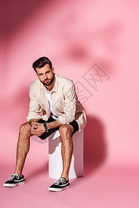 穿着暑期衬衫和短裤的时尚男子坐在粉红色图片