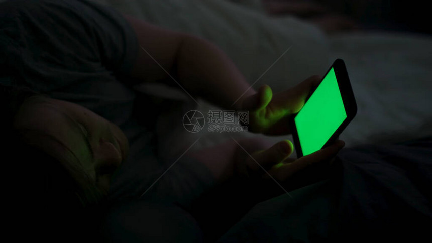 年轻人晚上在床上沉迷于带绿屏的智能手机图片