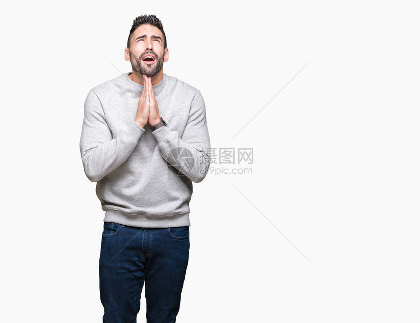 年轻英俊的男子穿着运动衫在孤立的背景下乞讨和祈祷图片