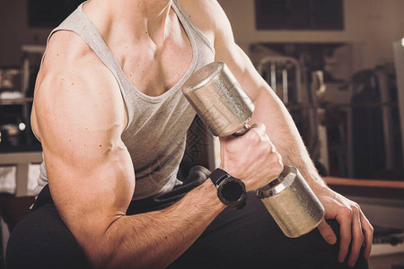 在Biceps与哑铃一起在健身房锻炼的肌肉男T图片