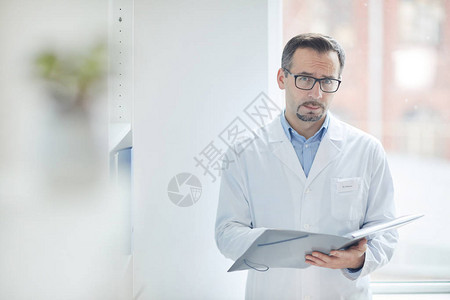 身穿白大褂的成年男医生在办公室填写医疗卡时站着看图片