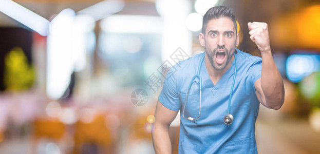 英俊的年轻医生外科医生在孤立的背景下愤怒和疯狂地举起拳头沮丧和愤怒图片