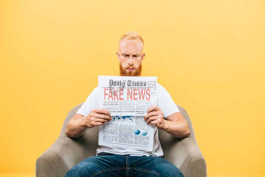 坐在扶手椅上背着假新闻阅读报纸的男子图片