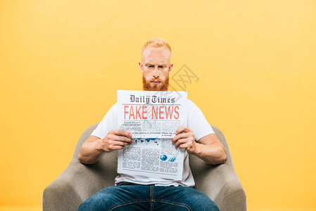 坐在扶手椅上背着假新闻阅读报纸的男子背景图片