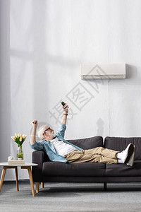 年长男子在沙发上举起遥控空调器的遥控器图片