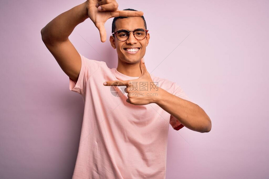 身穿轻便T恤和眼镜的非洲帅哥美国人在粉红色背景上笑着微笑图片