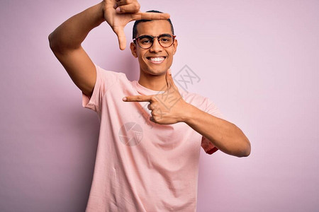 身穿轻便T恤和眼镜的非洲帅哥美国人在粉红色背景上笑着微笑背景图片