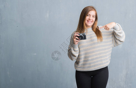 灰色垃圾墙上的年轻成年女用老式相机拍照图片
