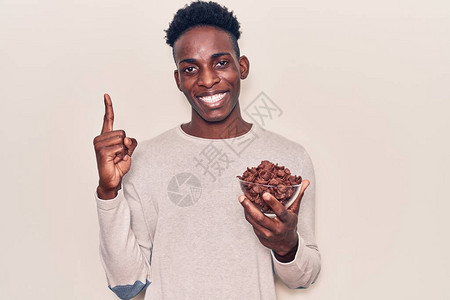年轻非洲美国人拿着巧克力麦片微笑着一个想法或问题用快乐的面孔指着手图片