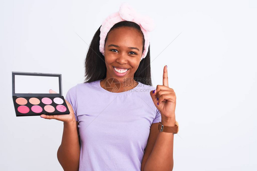 年轻的非洲美籍女在孤立的背景中拿着化妆盘子惊讶地发现一个想法或问题用快乐的面孔指着手图片