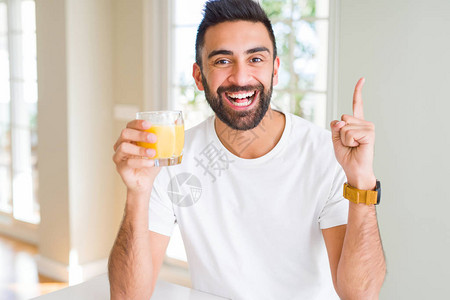 喝健康橙汁的英俊惊讶于一个想法或问题与快乐的面孔对图片