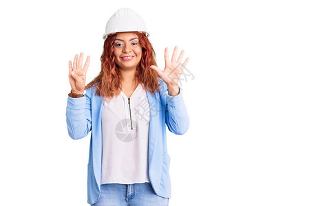 年轻拉丁女人穿着建筑师的硬礼服露面用指头着九号手指笑图片