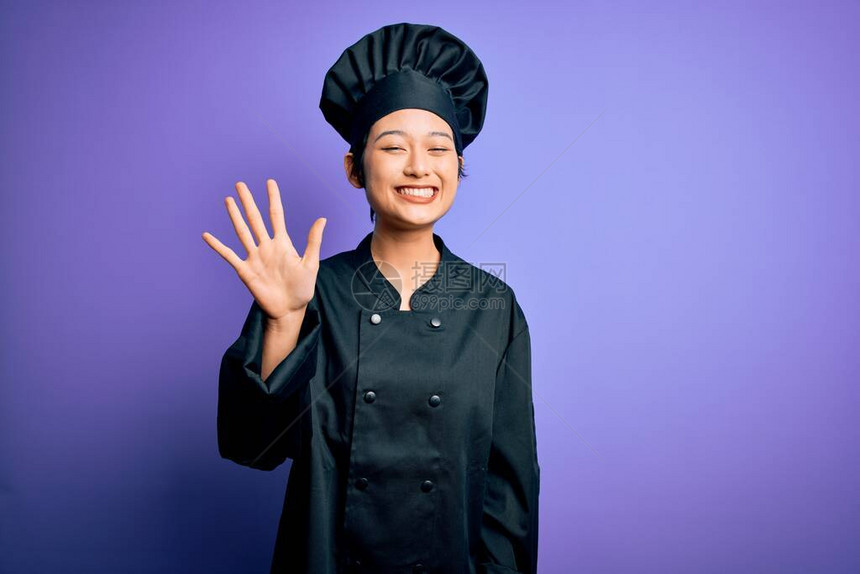 年轻的厨师女厨师身穿烹饪服戴着紫色背景的帽子举起五指头满怀自信图片