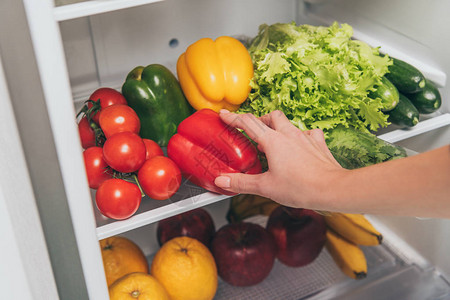 妇女用新鲜蔬菜和水果从冰箱中取出胡椒图片