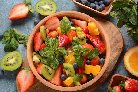 木制背景上的健康新鲜多彩水果沙拉碗顶视图草莓蓝莓甜樱桃猕猴桃的水果沙拉素食概念背景图片