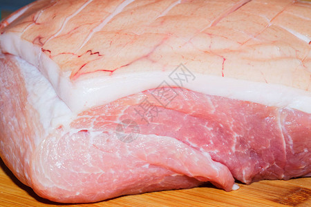 木制背景上带皮的生烤猪肉的特写图片