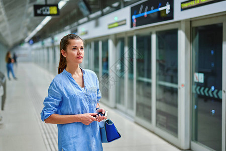 在地铁站拿着手提包等待火车到达的年轻女子图片