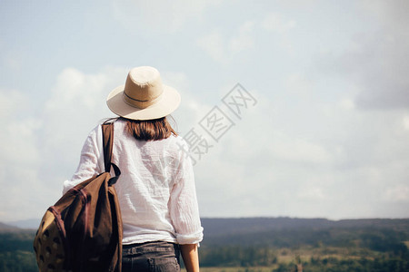 背着包旅行的时髦女孩站在阳光明媚的山顶上图片