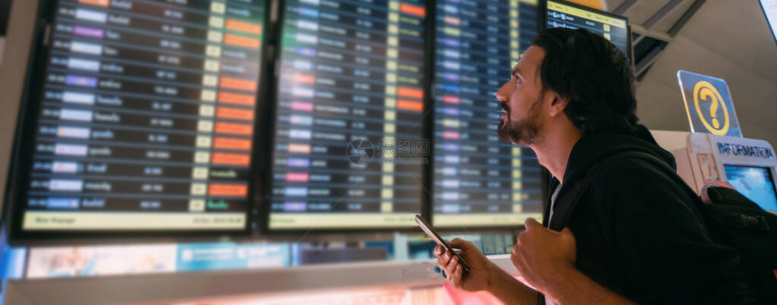 一个背着包的年轻人在候机楼的屏幕上查看航班时刻表图片