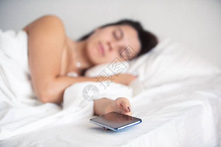 女人睡在她的手智能手机的床上电话里背景图片