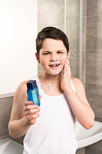 不满的前十几岁男孩在卫生间脸上涂抹润肤图片