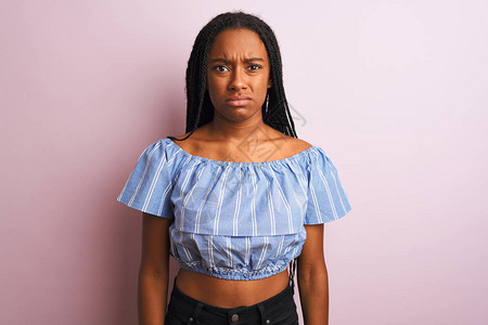 身穿条纹T恤的非裔美国妇女站在孤立的粉红色背景怀疑和紧张之上图片