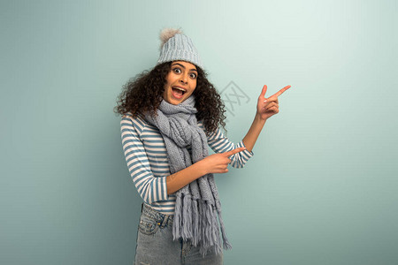 身戴温暖帽子和围巾的两种族女孩在用手指对着灰色背景时图片