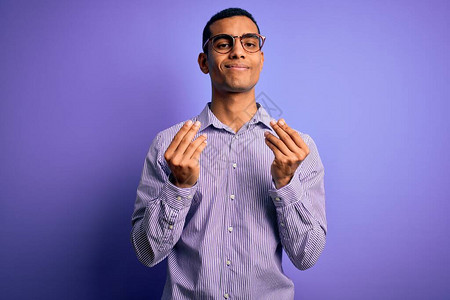 身穿紫色背景条纹衬衫和眼镜的帅气非洲裔美国人用手做金钱手势图片