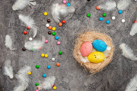 复活节背景多色鸡蛋在巢中糖果和羽毛散布在灰图片