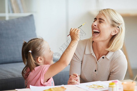 快乐的年轻女子在房间里涂油漆时和孩子玩得开心图片