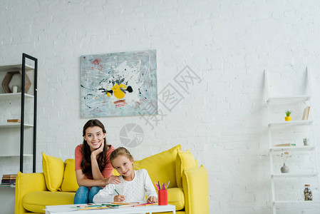 快乐的保姆坐在黄色沙发上靠近孩子在客厅图片
