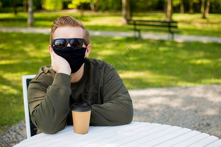 戴着保护黑色面具的悲伤人坐在咖啡馆的桌子旁防护戴着面具的男人在图片