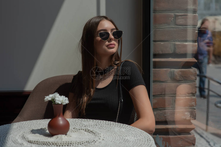 咖啡馆里的时尚女人坐在椅子上的女士戴眼镜的女孩戴着黑眼镜的咖啡馆里的女孩在咖啡店的早晨阳光下图片