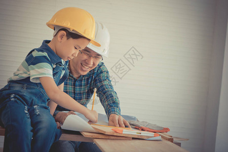 小男孩正在学习成为建筑工匠从他的技艺师父亲图片