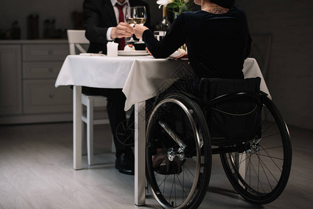 在浪漫晚餐期间和男朋友一起喝着白葡萄酒杯的轮椅女图片