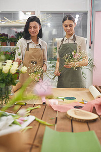 两位创意年轻女在花店工作时布置花束和花卉作品的垂直肖图片