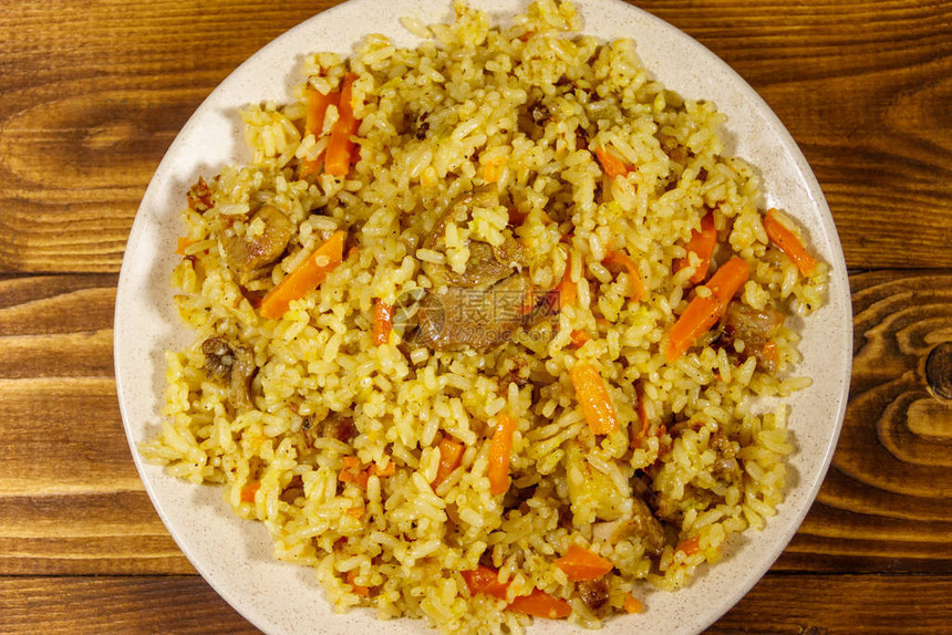 木桌上的盘子里有肉米饭胡萝卜和洋葱的图片