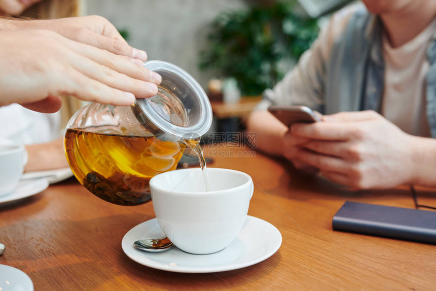 拿着茶壶的手把草药茶倒进白瓷杯子的人在咖啡馆和大学图片